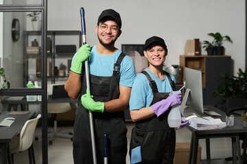 Portrait of colleagues in uniform smiling at camera while doing cleaning in team in office
