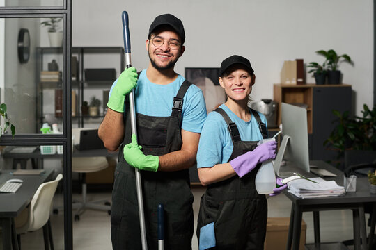 Portrait of colleagues in uniform smiling at camera while doing cleaning in team in office - Powered by Adobe
