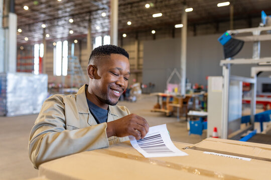 African American man peeling barcode label at warehouse packing station, with packaging machinery - Powered by Adobe