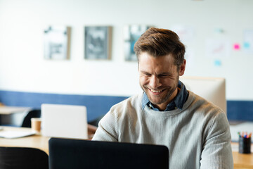 Man sitting at wooden desk in modern coworking space, working on black laptop with coffee cup