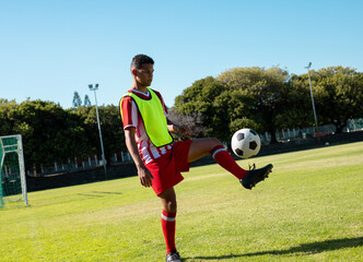 Male soccer player juggling soccer ball on soccer pitch, with fluorescent yellow bib, copy space
