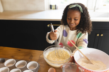 African American girl whisking batter in home kitchen, with glass bowl and muffin tin, copy space