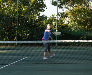 Young adult woman swinging racket and volleying tennis ball over net on outdoor court at park