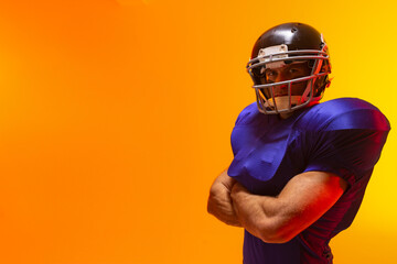 Male football player standing arms crossed in studio, with helmet and shoulder pads, copy space © wavebreak3