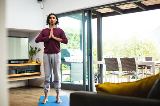 Non-binary person doing yoga prayer pose on blue mat in modern living room, by sliding doors