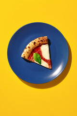 Slice of delicious pizza margherita resting on blue plate with yellow background