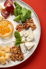 Plate combining different cheeses, walnuts, grapes, honey and mint on red background