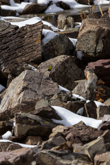 Snow-covered rocks with small bird perched in rugged terrain during winter afternoon in remote location