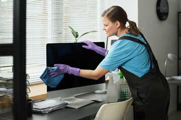 Woman using rag to clean computer screen during wet cleaning in office