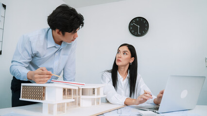 Professional male asian architect using ruler to measure house model length while young beautiful...