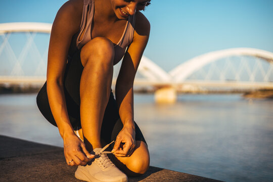 Athletic Woman Tying Her Running Shoes Near a Scenic Bridge - Powered by Adobe