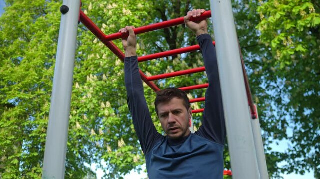 Male athlete training on red monkey bars in outdoor gym. Man doing sport exercises in open air park for wellness and body control. Concept of fitness, endurance and healthy lifestyle