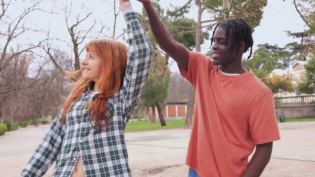 Happy interracial couple dancing and holding hands in a park, enjoying a romantic moment together