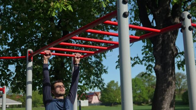 Male athlete training on red monkey bars in outdoor gym. Man doing sport exercises in open air park for wellness and body control. Concept of fitness, endurance and healthy lifestyle