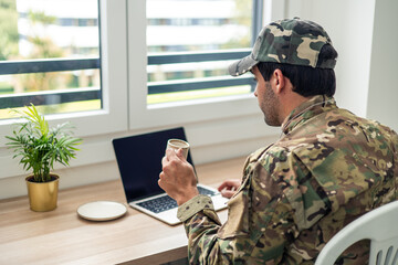 Fototapeta premium American soldier working from home drinking coffee and using laptop