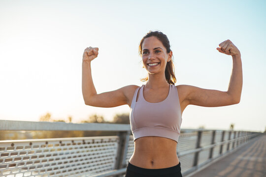 Smiling Fit Woman Flexing Arms in Athletic Wear During Outdoor Workout