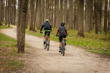 Naklejka premium Two women ride bicycles on a dirt trail through a forested park area, enjoying an outdoor activity surrounded by tall trees and nature.