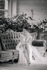 Bride in a lace wedding dress sits gracefully on a vintage sofa in a classic interior, captured in elegant black and white..