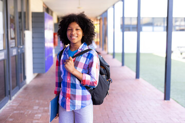 Obraz premium African American boy child standing in school walkway, carrying black backpack, holding blue folder
