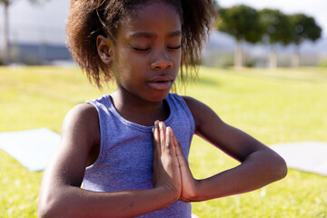 African American child girl meditating on yoga mat in public park, finding inner peace