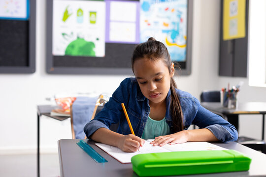 8-year-old girl writing in elementary school classroom, using yellow pencil and teal ruler