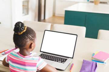 African American child using laptop and drawing at home kitchen table with pencils, copy space