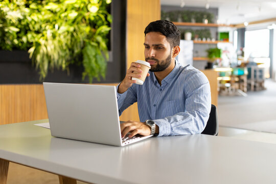 Man working on silver laptop in coworking space, sipping coffee cup and wearing watch, copy space