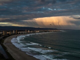 Dramatic sunset over coastal city with waves crashing and clouds gathering on a late afternoon