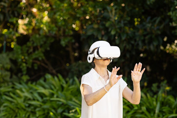 Senior Asian woman experiencing virtual reality in lush outdoor garden, with white VR headset