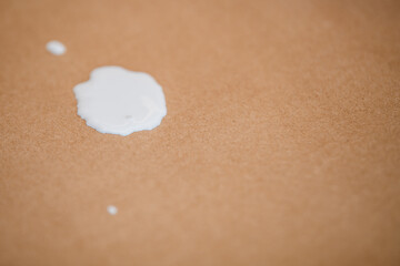 Close up of a white paint splatter spilled on a brown kraft paper surface showing the texture and contrast between the paint and the background.