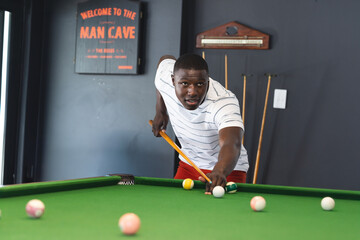 Young African American man shooting pool on green pool table in man cave, with cue stick