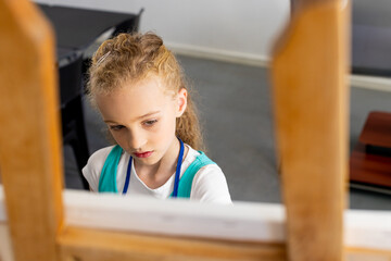 Female child painting on canvas behind wooden art easel in art studio, featuring black table