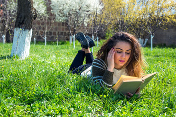 Beautiful girl lies on meadow and reads the book