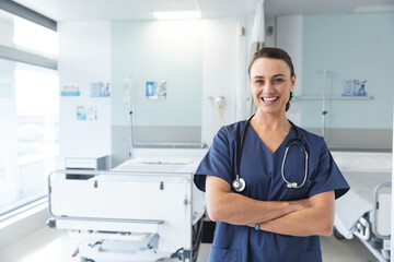 female nurse standing with arms crossed and smiling in hospital ward with IV stand, copy space