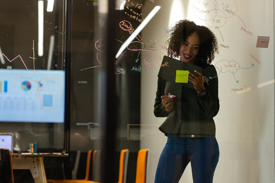 woman writing on glass wall in modern conference room with pink marker and tablet, copy space