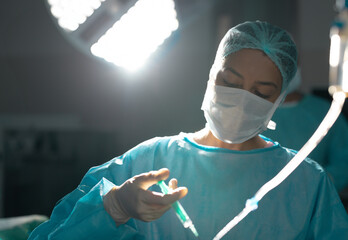 Young female surgeon with mask preparing syringe under surgical light with tubing in operating room