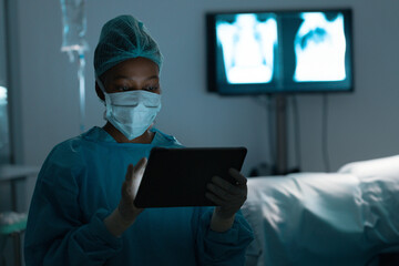African American female surgeon reviewing tablet in dim hospital room with IV stand, copy space