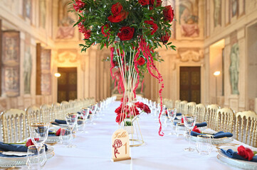 Sophisticated wedding table arrangement in a grand palace hall with frescoed walls, ornate chandeliers, and lush red floral centerpieces for luxury event inspiration