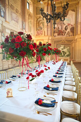Upscale event floral decor with dramatic red rose centerpieces in a richly decorated historic interior, featuring marble-like frescoes and vintage gold chairs