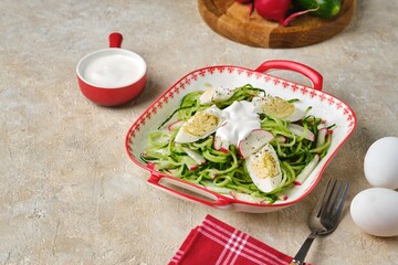 Spring cucumber and radish salad with boiled egg and sour cream dressing in a deep plate on a light concrete background. Vegetarian recipes.
