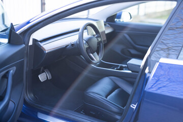 Steering wheel of a electric vehicle, interior cockpit, electric buttons, digital speedometer, front seats, textile, windows, console, gear shift. Car dashboard with a digital touchscreen