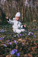 Little girl in violet boots and blue overall sitting in spring blooming forest