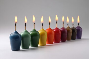 A vibrant row of colorful candles burns brightly against a soft, gray background, creating a warm, celebratory atmosphere with their flickering flames, ideal for birthdays