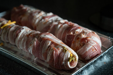Two large meatloaf rolls are wrapped in strips of bacon, showcasing a rich stuffing with herbs and...
