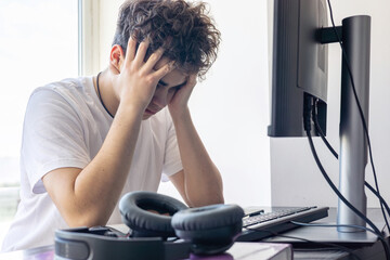 Stressed teenager with head in hands while studying at home. Distance learning, exam anxiety,...