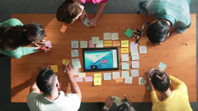 Top down view of programmer brainstorming and planning about web design while looking at tablet wireframe prototype. Aerial view of skilled developer team talking about digital application. Symposium.