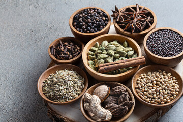 Set of various whole warming Indian spices in wooden bowls on a gray background vertical shoot. Healthy food, alternative medicine, ayurvedic spice treatment.