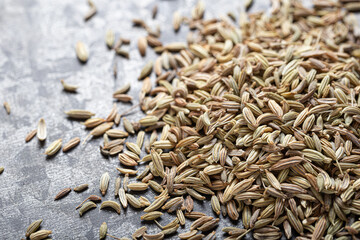 A close-up of dried fennel scattered on a textured light gray surface, Indian spice