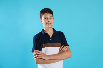 Portrait of teenage boy with crossed arms on light blue background
