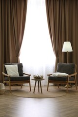 Comfortable armchairs near window with stylish curtains in living room. Interior design